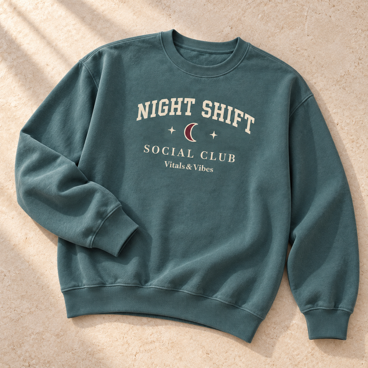 Night Shift crewneck in Blue Spruce, laid out on a table, showing the Night Shift moon, stars and Social Club print.