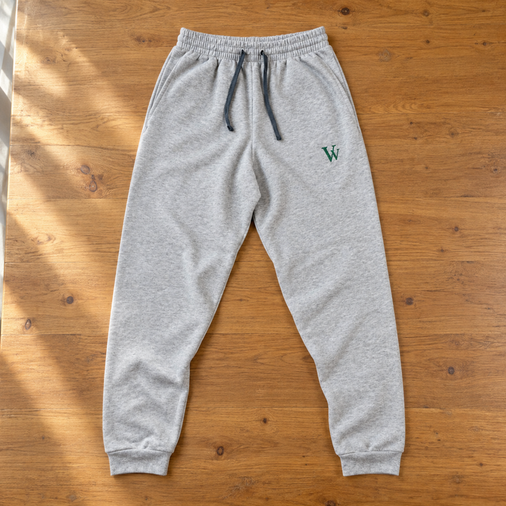 Athletic Heather embroidered joggers laid on a wood table, showing dark drawcords, flat cuff bands and a small green VV on the left thigh.