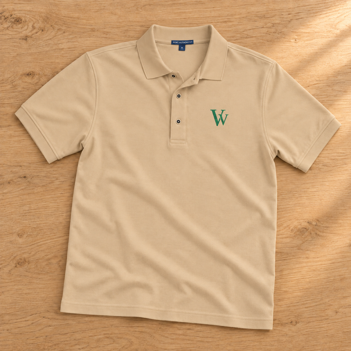 Stone Port Authority polo laid on warm oak, showing green VV monogram embroidery and three-button collar.
