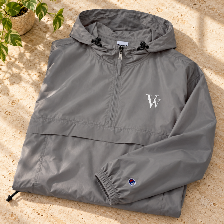 Graphite Champion anorak folded on pale stone, showing the white VV embroidery, hood and sleeve emblem.