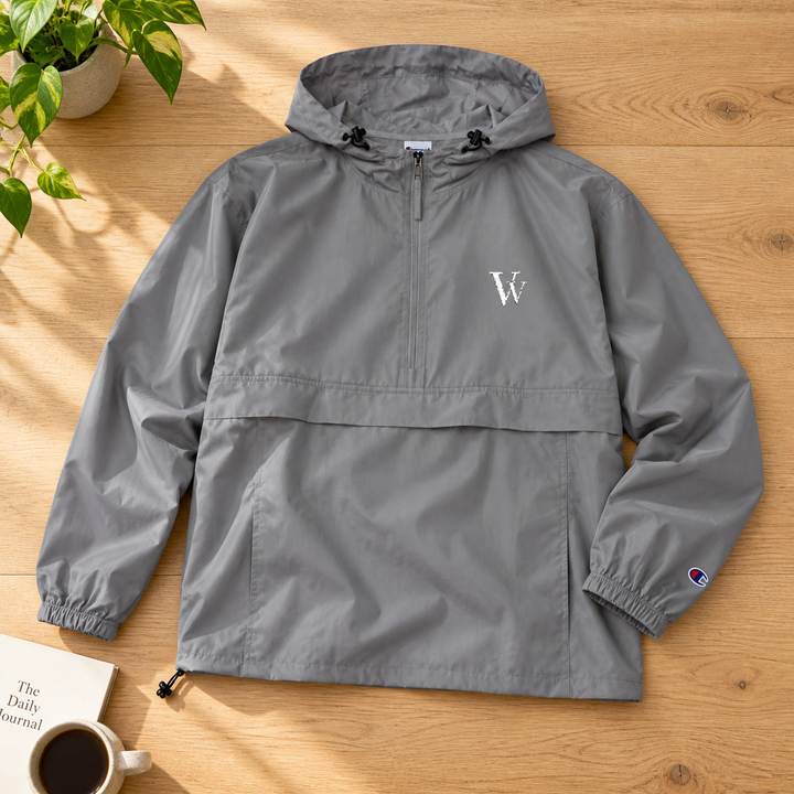 Graphite Champion packable anorak on a wood table, showing white VV embroidery, hood and drawcord hem.