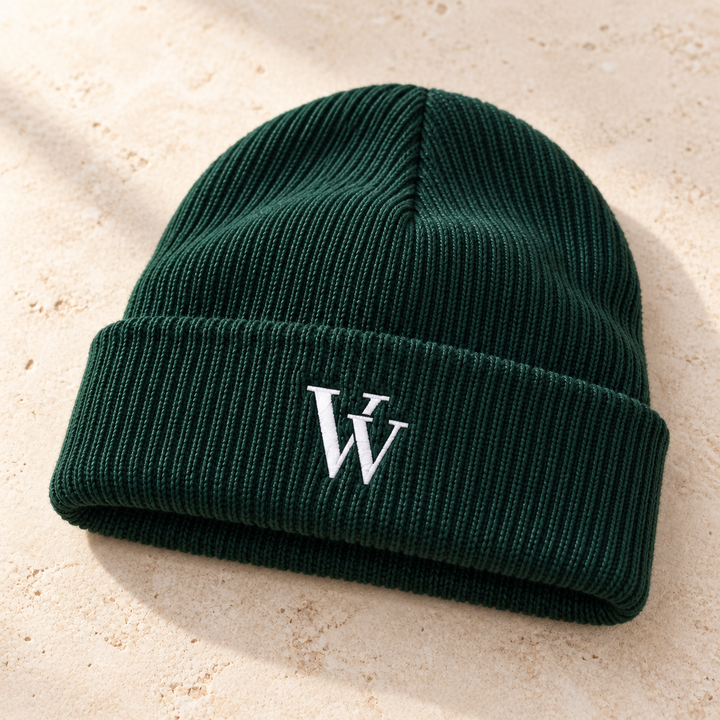 Closer view of the Spruce cuffed beanie resting on ivory stone, showing the rib-knit texture, single folded cuff and white VV embroidery.