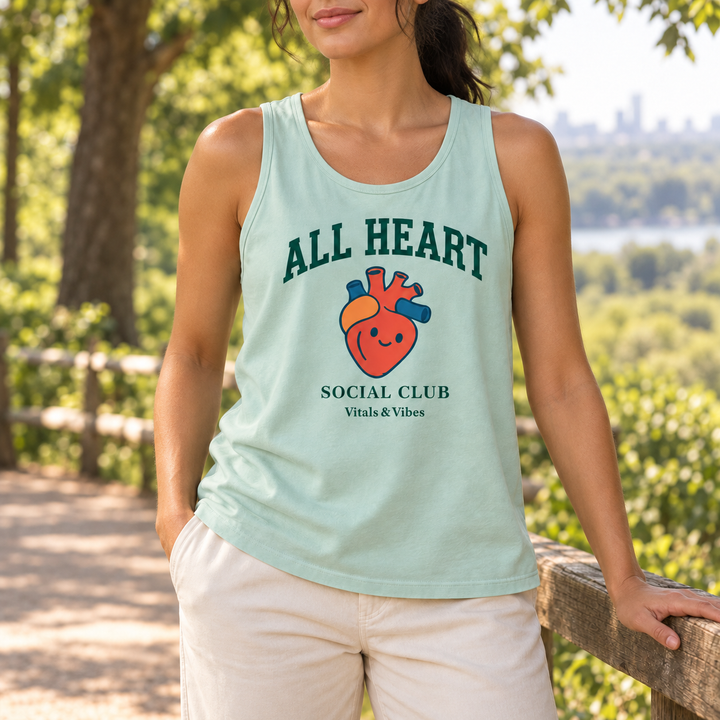 Woman at a park railing wearing a pale mint All Heart tank with a smiling anatomical heart and Social Club lettering.