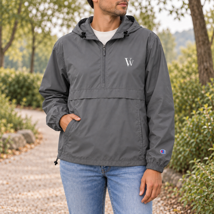 Man wearing the Graphite Champion packable anorak with white VV embroidery, front flap and drawcord hem on a park path.