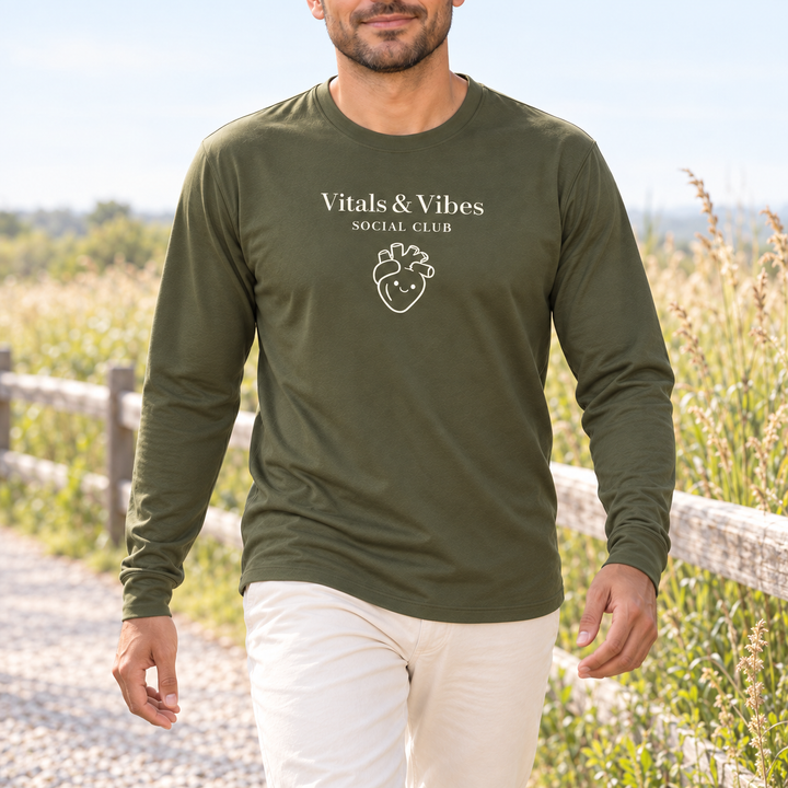 Man walking on a pale gravel path beside a timber fence and meadow grasses in an olive Vitals & Vibes performance long sleeve.