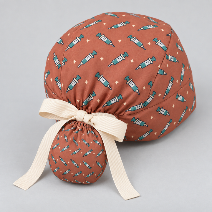 Needle ponytail scrub cap — studio mockup showing the printed cap and cream ties.