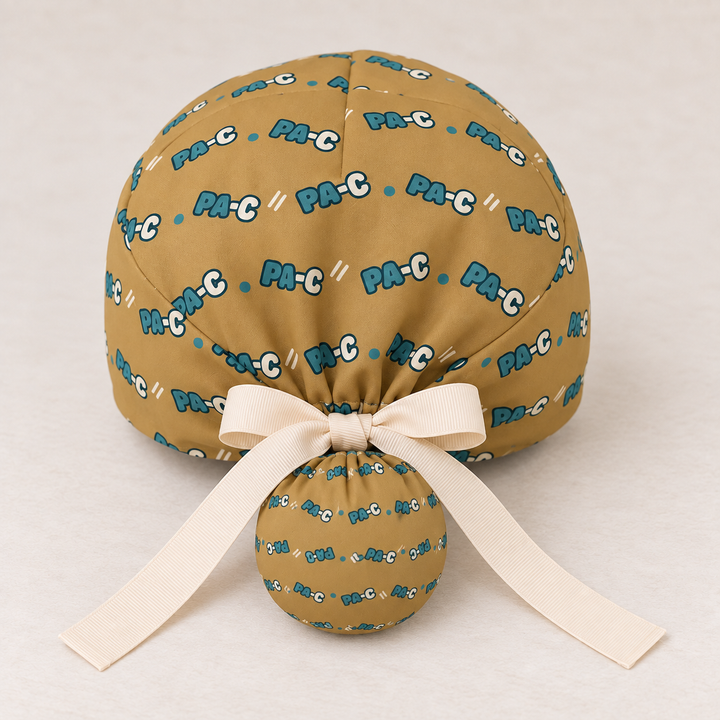 PA-C ponytail scrub cap — studio mockup showing the printed cap and cream ties.