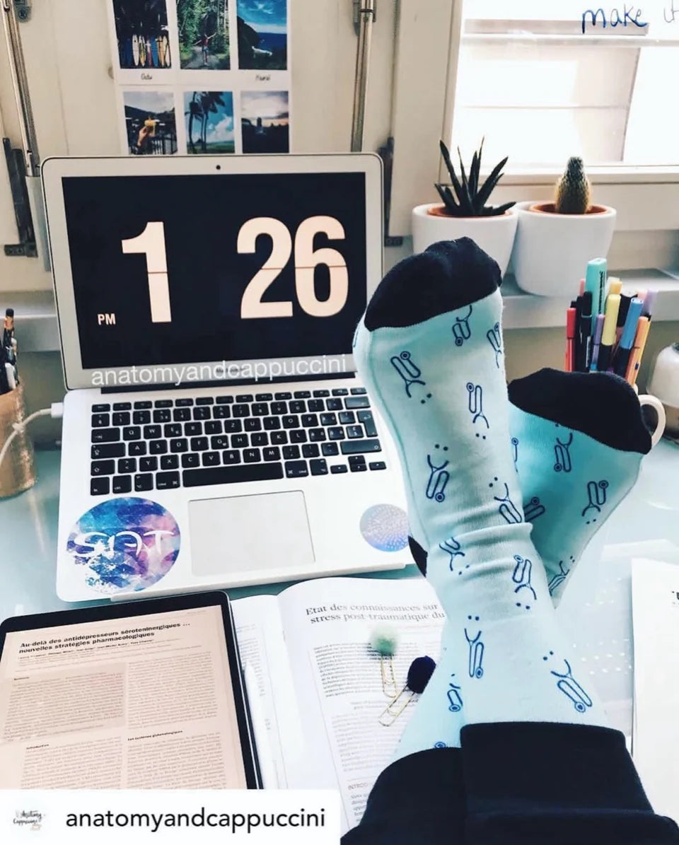 Stethoscope-patterned socks propped up beside medical reading and a laptop at anatomyandcappuccini's study desk.