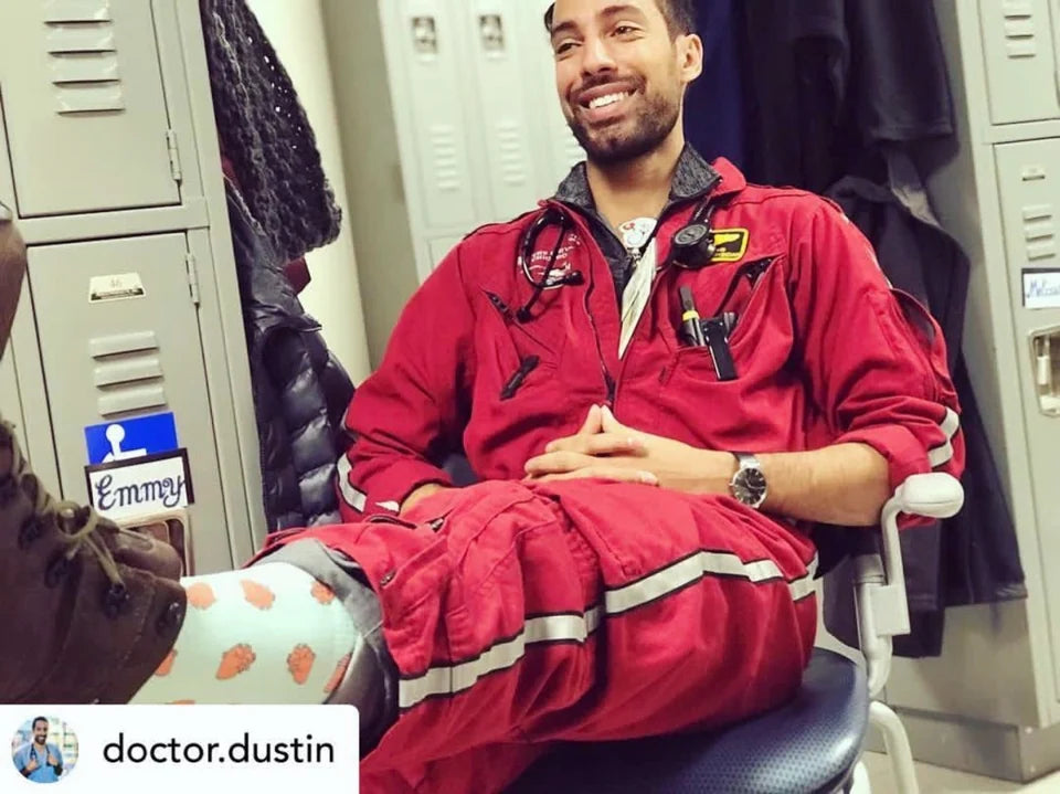 Doctor Dustin wearing red medical workwear and coral heart-patterned socks above boots, from the 2019 outreach archive.