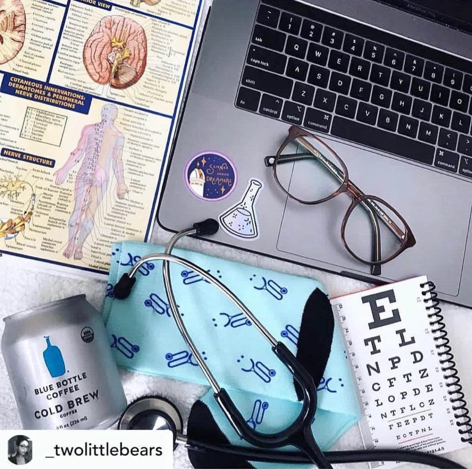 Blue stethoscope-patterned socks beside anatomy notes, glasses, and a laptop, photographed by _twolittlebears.